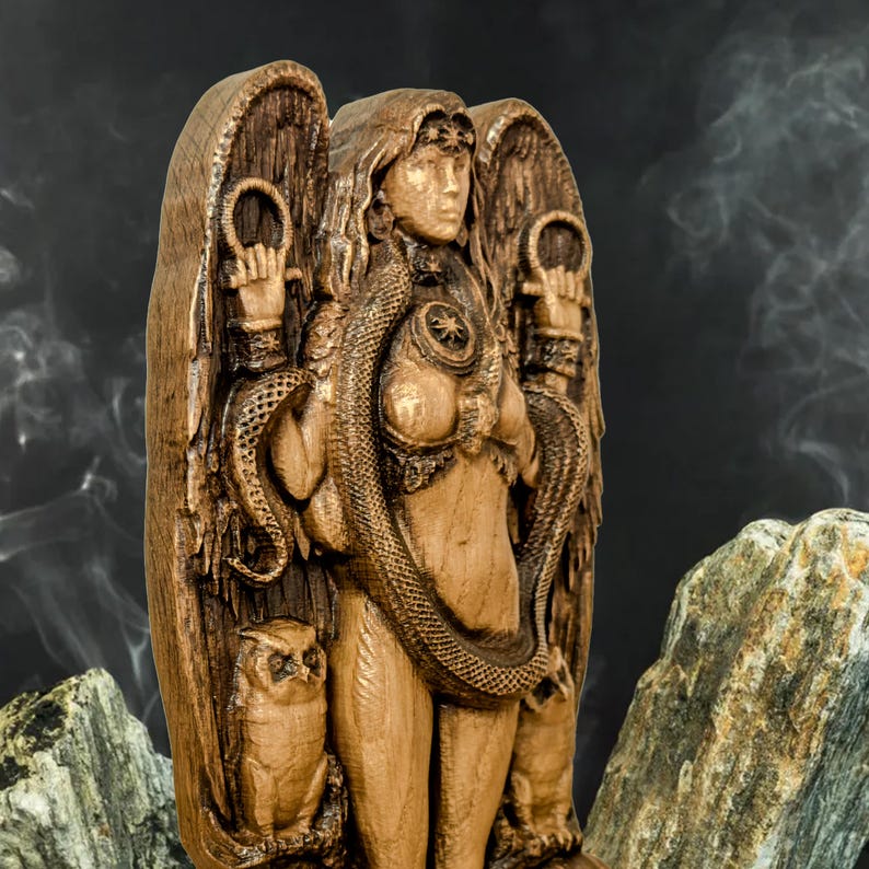 May include: A wooden sculpture of a female figure with wings, a snake wrapped around her body, and owls on either side. The figure is carved in a detailed style and has a warm brown color.