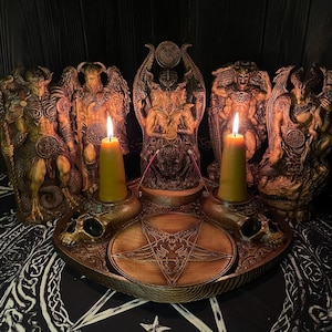 Può includere: Un vassoio da altare circolare in legno con un pentagramma inciso al centro, due portacandele a forma di teschio con candele a colonna gialle accese e cinque dettagliate statuette demoniache disposte a semicerchio dietro il vassoio.