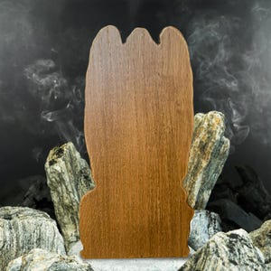 May include: A wooden cutout of a hand with a brown wood grain finish. The cutout is standing on a bed of charcoal and rocks.