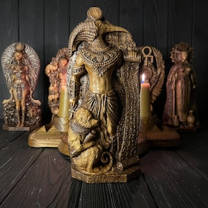 Puede incluir: Una escultura de resina de color marrón dorado de la deidad egipcia Thot, representada con cabeza de ibis y un babuino a los pies, de pie junto a un pergamino. La figura presenta tallas intrincadas y se exhibe junto a otras estatuas egipcias.