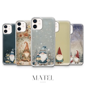 Peut inclure: Cinq coques de téléphone avec des illustrations de gnomes festifs. Chaque coque présente un design différent, notamment des gnomes avec des lanternes, dans des scènes hivernales et des motifs floraux. Les coques sont transparentes, avec la marque "MATEL" en bas.
