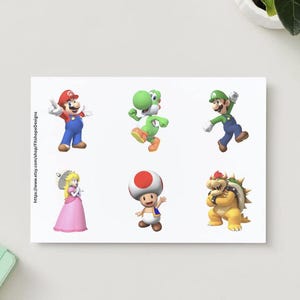 May include: A white card featuring six colorful illustrations of characters from the Super Mario video game series. The characters include Mario, Luigi, Yoshi, Princess Peach, Toad, and Bowser. The Etsy shop URL is visible on the card.