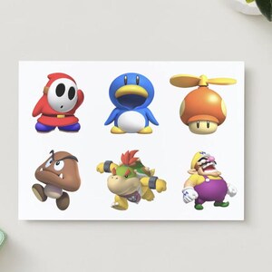 May include: A white card featuring six colorful cartoon characters from the Super Mario video game series. The characters include Shy Guy, a blue penguin, a mushroom with a propeller, a Goomba, a Koopa, and Wario.