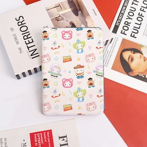 Könnte beinhalten: Eine cremefarbene Tablet-Hülle mit einem sich wiederholenden Muster aus Zeichentrickfiguren, Sternen und Schleifen. Die Hülle enthält Charaktere wie Hello Kitty, Aliens und Mr. Potato Head. Der Text "Kitten Story" ist ebenfalls sichtbar.