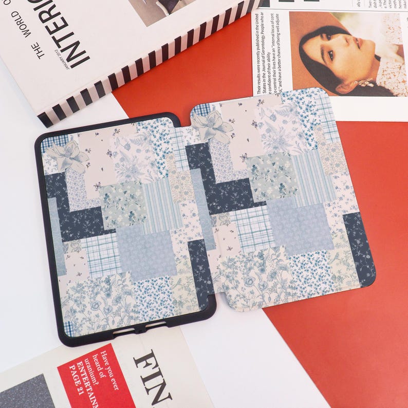 May include: Two matching tablet cases with a patchwork design in shades of blue, white, and navy. One case is open, revealing the interior, while the other is closed. The cases are on a red surface with magazine pages.