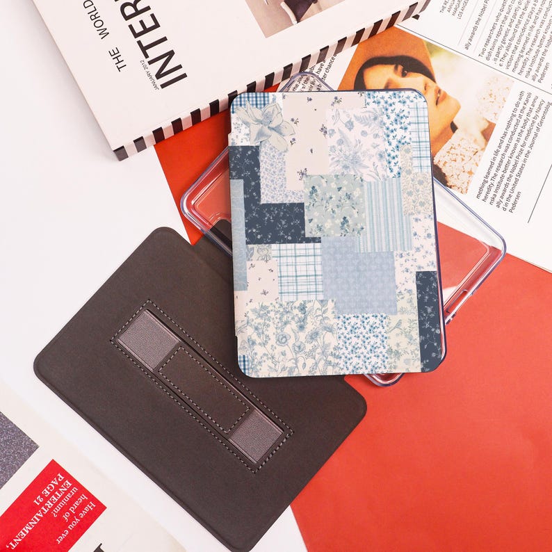 May include: A rectangular case with a patchwork design in shades of blue and white, featuring floral and plaid patterns. A brown case with a gray strap is also visible, along with a clear plastic case and a magazine.
