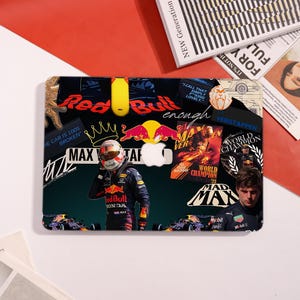 May include: A black and green laptop skin featuring a collage of Red Bull Racing imagery. The design includes the Red Bull logo, a Formula 1 driver, and the text "MAX VERSTAPPEN" and "WORLD CHAMPION".