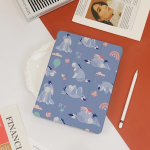 May include: A blue tablet case featuring a pattern of Eeyore characters, clouds, rainbows, and stars. The case has a smooth finish and is surrounded by other items, including a white stylus and magazines.