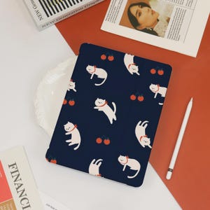 May include: A navy blue iPad case with a repeating pattern of white cats and red cherries.