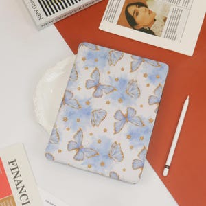 May include: A white laptop case with a blue and gold butterfly pattern. The case has a subtle watercolor effect and features gold stars scattered throughout the design.