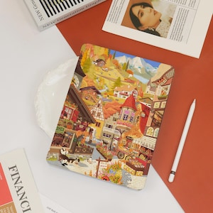 May include: A colorful tablet case featuring a detailed illustration of a European village scene with houses, mountains, and a clock tower. A white stylus rests nearby. The case is on a red surface with a white plate and magazines.