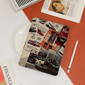 May include: A tablet case featuring a collage of car-themed images and text, including "NISSAN", "HAMILTON", and "McLAREN SENNA". The design incorporates various car illustrations and magazine-style layouts in a mix of colors. A white stylus is placed nearby.