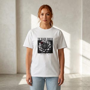 May include: A white short-sleeved t-shirt featuring a black and white graphic of a dahlia flower with a small red accent. The text reads THE BLACK DAHLIA above the flower and LOS ANGELES 1947 below the flower in a simple black sans-serif font.