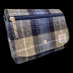 May include: A rectangular pouch featuring a blue, tan, and dark brown plaid pattern. The bag has a top zipper with a silver-toned metal pull featuring an intricate Celtic knot design, a front flap with a single silver snap, and a Harris Tweed label.