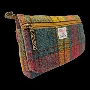 May include: A rectangular zippered pouch made of multicolored plaid wool fabric in shades of yellow, teal, and red. It features a gold-toned metal zipper with a decorative Celtic knot pull and a white Harris Tweed label sewn on the front.