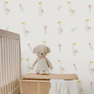 May include: A white nursery wall with a repeating pattern of pink flowers and white geese. A stuffed dog sits on a wicker storage bin in front of the wall.