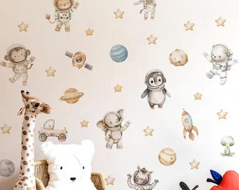 May include: A collection of watercolour wall stickers depicting animals in space suits, such as a lion, monkey, giraffe, penguin, elephant, and zebra, alongside planets, stars, and a rocket. The stickers are in soft pastel colours, creating a whimsical space theme.