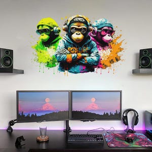Może przedstawiać: Naklejka ścienna przedstawiająca trzy stylizowane małpy w słuchawkach i okularach przeciwsłonecznych. Małpy są przedstawione w żywych kolorach i otoczone kolorowymi plamami farby. Obraz znajduje się nad biurkiem z dwoma monitorami komputerowymi, głośnikami i klawiaturą.