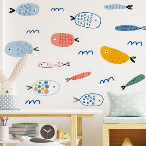 Pode incluir: Uma parede branca decorada com autocolantes de peixes de desenhos animados coloridos em várias formas e padrões. Os peixes são em tons de azul, laranja, amarelo e verde, com barbatanas caudais pretas. Também estão presentes formas de ondas azuis.
