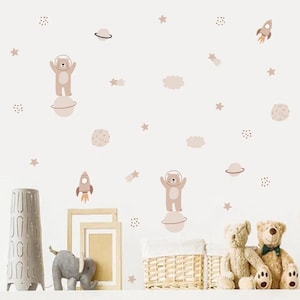 May include: A set of brown bear astronaut wall decals featuring planets, stars, and rockets. The decals are ideal for a nursery or child's room.