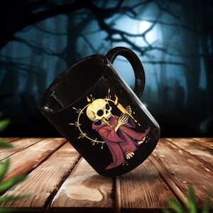 Gothic skull monk mug featuring a creepy undead priest holding a candle with a glowing halo. This high-resolution PNG design is perfect for horror lovers, gothic decor, Halloween gifts, and dark fantasy aesthetics. The black ceramic mug adds an eerie yet stylish touch, making it ideal for witchy coffee lovers, occult fans, and alternative fashion enthusiasts.