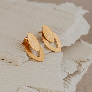 May include: A pair of gold leaf-shaped earrings with a textured finish. The earrings are layered, with one leaf shape overlapping the other.