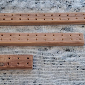 May include: Three wooden dowels with evenly spaced holes drilled into them. The dowels are different lengths and are arranged in a row from longest to shortest.