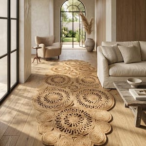 Puede incluir: Una alfombra de pasillo de fibra natural con un diseño circular, colocada sobre un suelo de madera. El patrón de la alfombra presenta círculos repetidos con detalles intrincados. La habitación tiene una paleta de colores neutros con un sofá, un sillón y una mesa de centro de madera.