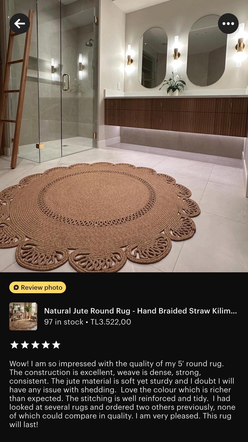 May include: A round, natural jute rug with a braided design. The rug has a scalloped edge and is approximately 5 feet in diameter. It is placed on a tiled floor in a bathroom setting.