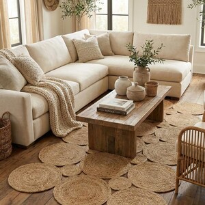 May include: A living room scene featuring a large, cream-colored sectional sofa, a wooden coffee table, and a collection of round, woven jute rugs. Decorative vases and a woven wall hanging add to the room's neutral, natural aesthetic.