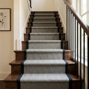 May include: A wooden staircase with grey carpeted steps and a black border. The stairs have a dark wood handrail and black metal balusters. A framed botanical print hangs on the wall.