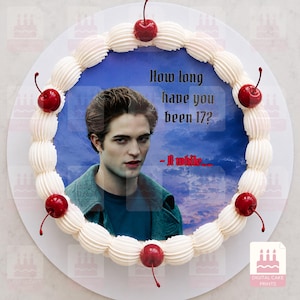 May include: A round cake topper featuring a portrait of a man with dark hair wearing a teal jacket against a blue cloudy sky. The text reads, "How long have you been 17? - A while...." The image is bordered by white piped frosting and red cherries.