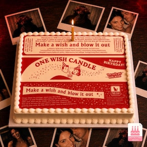 May include: A square white birthday cake with a red and white graphic print resembling a product box. The text reads "ONE WISH CANDLE" and "Make a wish and blow it out." A single lit gold candle is centered on top of the cake frosting.