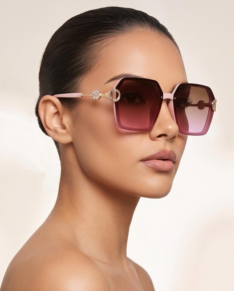 May include: Pink and gold-toned sunglasses with a geometric frame and gradient lenses. The sunglasses feature decorative accents on the temples. The lenses transition from a dark to a lighter shade of pink