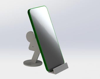 May include: A silver phone stand with a green-edged screen. The stand has a circular base and a figure-shaped support. The phone screen is angled and appears to be a smartphone.