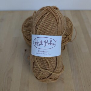 Può includere: Due matasse di filato marrone dorato avvolte in un'etichetta di carta bianca. L'etichetta riporta il testo Knit Picks, Essential e Gold Kettle Hand-Dyed in lettere marrone scuro. Il filato ha un aspetto ritorto e una tonalità calda e terrosa.