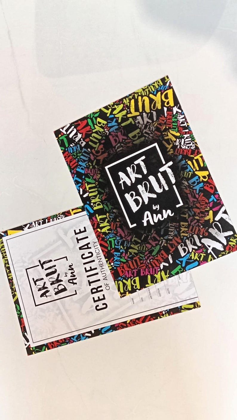 May include: Two rectangular art prints and a certificate of authenticity. The art print has a black background with colorful text that says "ART BRUT" in a graffiti style. The certificate is white with the words "ART BRUT by Ann".