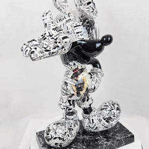 Pode incluir: Uma figura de Mickey Mouse em preto e branco vestindo uma roupa com padr&atilde;o preto e branco. A figura est&aacute; em p&eacute; sobre uma base de m&aacute;rmore preto e branco.