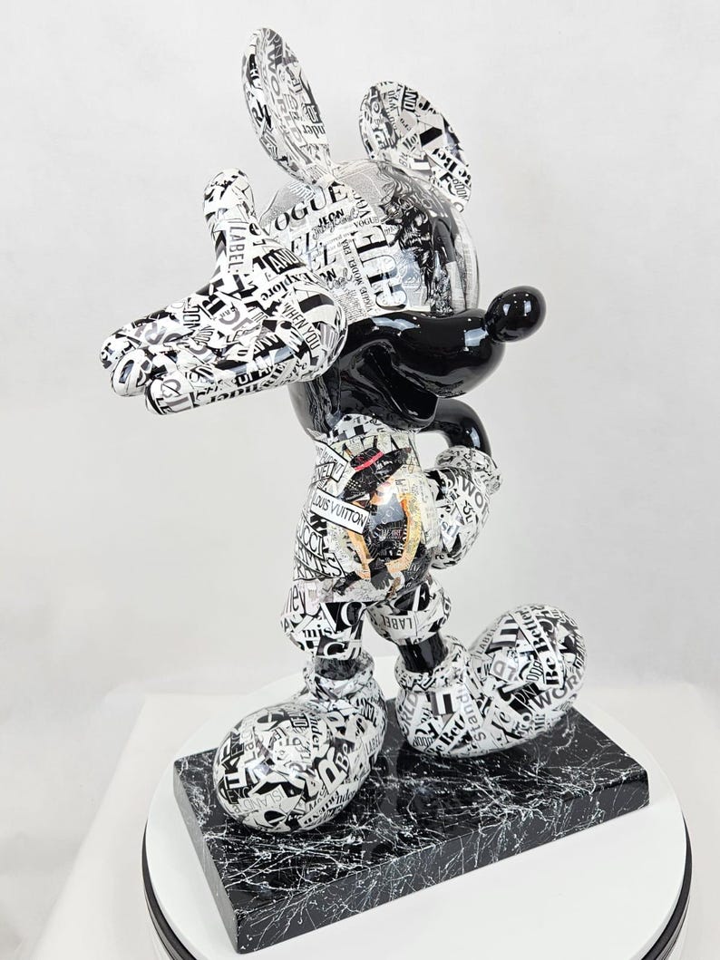 Pode incluir: Uma figura de Mickey Mouse em preto e branco vestindo uma roupa com padr&atilde;o preto e branco. A figura est&aacute; em p&eacute; sobre uma base de m&aacute;rmore preto e branco.