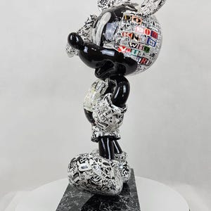Pode incluir: Figura de Mickey Mouse em preto e branco com um design de impress&atilde;o de jornal. A figura est&aacute; em p&eacute; sobre uma base de m&aacute;rmore preto.
