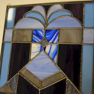 May include: A stained glass window with a geometric design featuring blue, purple, and brown glass pieces.