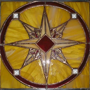 Pode incluir: Uma janela de vitral com uma estrela de cinco pontas com um centro vermelho, cercada por um círculo de vidro amarelo com uma borda de cobre.