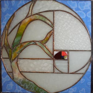 May include: A stained glass window with a circular design featuring a stylized tree branch with green and brown leaves. The background is a light blue with white clouds. The window is divided into sections with copper colored lead lines.