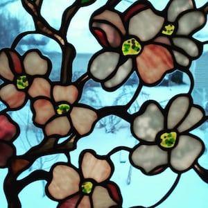 May include: A stained glass window depicting a branch of white dogwood blossoms with pink and green accents. The flowers are arranged in a cluster, with some overlapping. The background is a blurry blue.