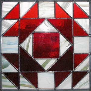 Pode incluir: Uma janela de vitral com um padrão geométrico vermelho e branco. O design apresenta um quadrado central rodeado por triângulos e quadrados.