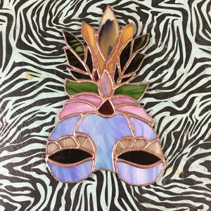 May include: A stained glass mask with a blue, purple, and pink design. The mask has a floral design on top with yellow, green, and brown accents.