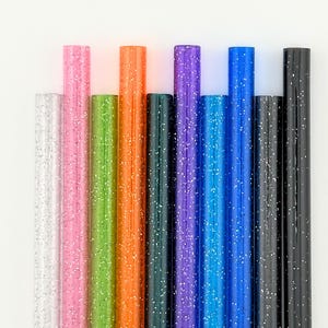 May include: A collection of colorful glitter pens in various shades, including silver, pink, green, orange, dark green, purple, blue, and black. Each pen is cylindrical and covered in glitter, creating a sparkling effect.