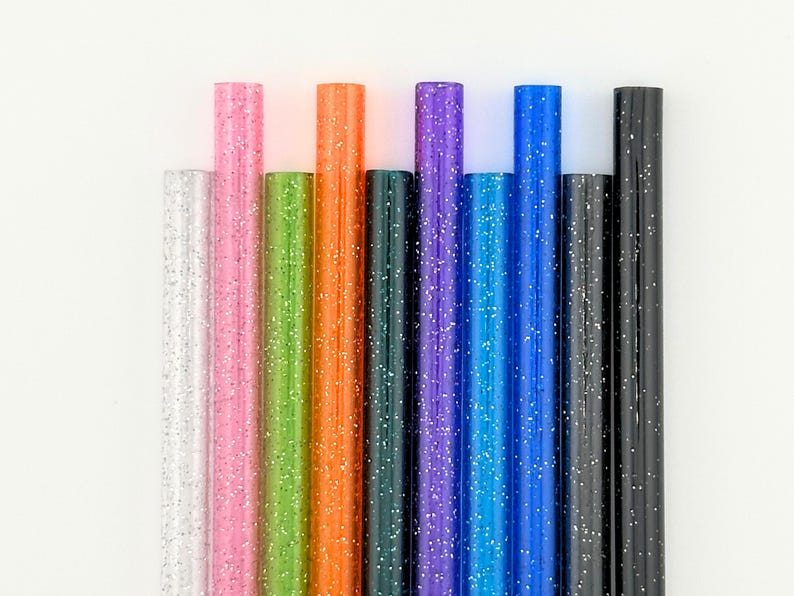 May include: A collection of colorful glitter pens in various shades, including silver, pink, green, orange, dark green, purple, blue, and black. Each pen is cylindrical and covered in glitter, creating a sparkling effect.