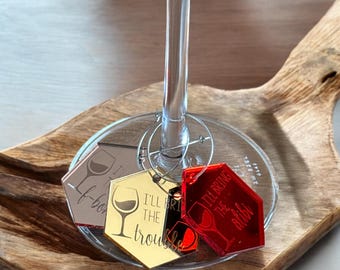 May include: Three hexagonal acrylic wine glass charms with gold and red mirrored finishes. The charms have the text "I'll bring the trouble", "I'll bring the bride", and "I'll bring the booze" on them.