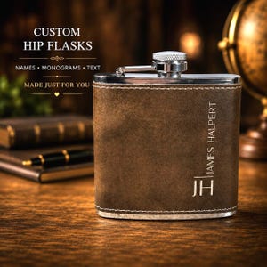 May include: A brown leather hip flask with a silver cap and trim. The flask has the name "JAMES HALPERT" and initials "JH" engraved on the front. The text "CUSTOM HIP FLASKS" is at the top.